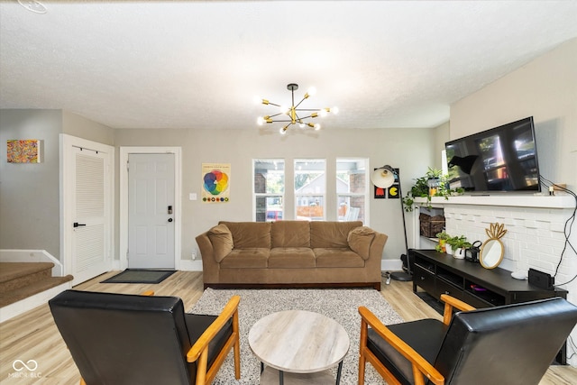 living room featuring a brick fireplace, a notable chandelier, light hardwood / wood-style flooring, and a textured ceiling