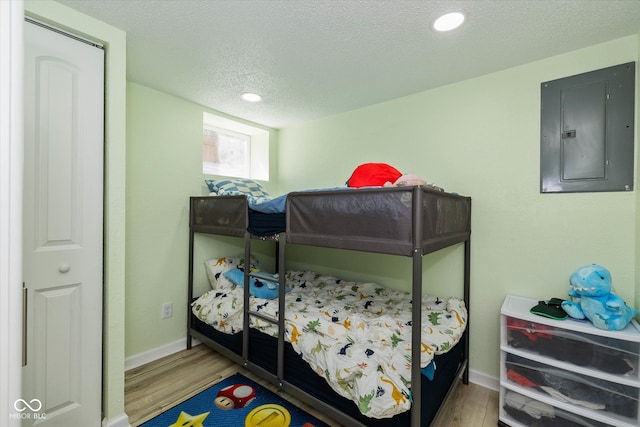 bedroom with wood-type flooring, a textured ceiling, and electric panel