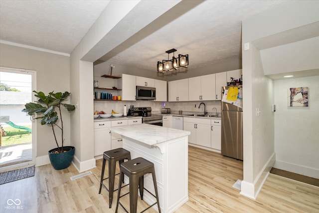 kitchen featuring white cabinetry, light hardwood / wood-style floors, appliances with stainless steel finishes, and hanging light fixtures