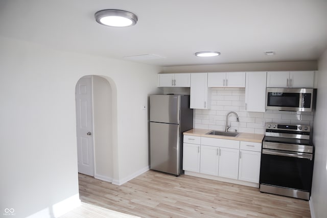 kitchen featuring sink, white cabinetry, stainless steel appliances, light wood-type flooring, and decorative backsplash