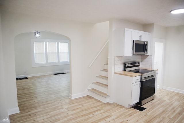 kitchen with appliances with stainless steel finishes, white cabinetry, light wood-type flooring, and tasteful backsplash