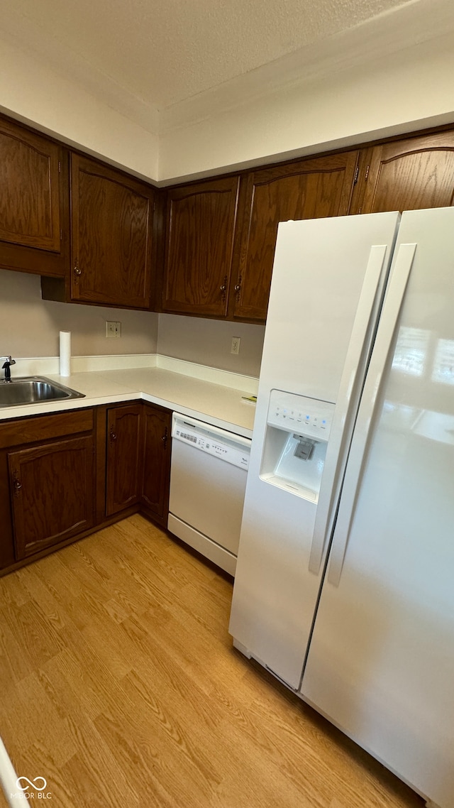 kitchen featuring dark brown cabinetry, white appliances, sink, and light hardwood / wood-style flooring