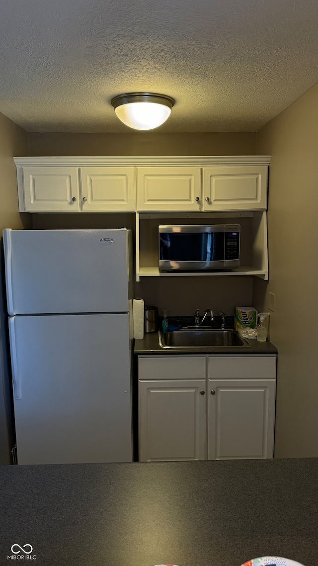 kitchen with a textured ceiling, white cabinetry, sink, and white fridge