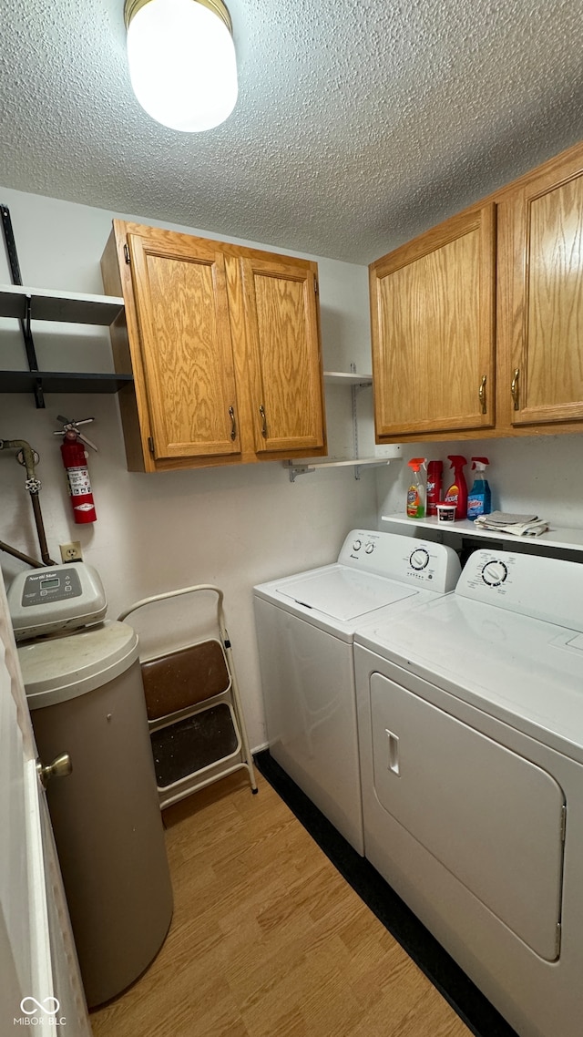 laundry area with a textured ceiling, washing machine and dryer, light hardwood / wood-style flooring, and cabinets