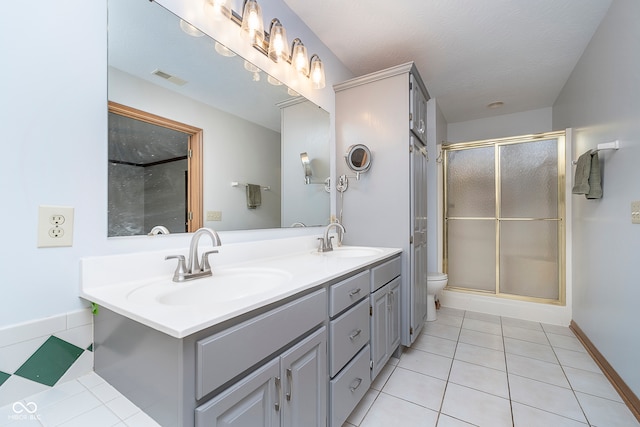 bathroom featuring vanity, a textured ceiling, tile patterned floors, toilet, and a shower with door