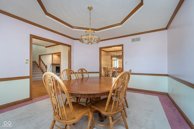 dining room featuring a raised ceiling, ornamental molding, a chandelier, and light colored carpet