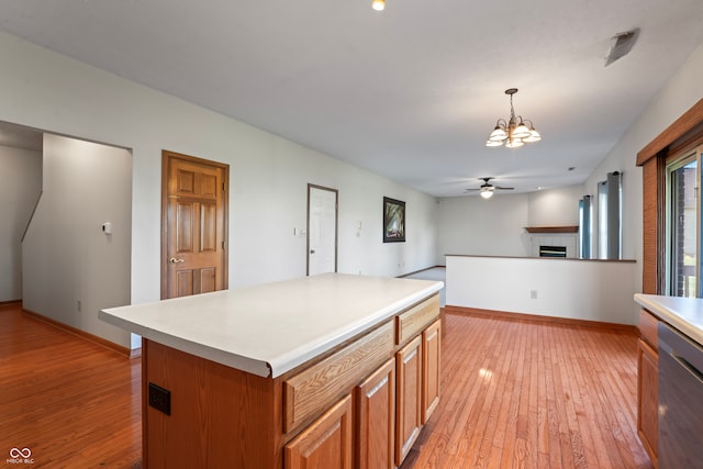 kitchen with dishwasher, a center island, pendant lighting, light hardwood / wood-style floors, and a tiled fireplace