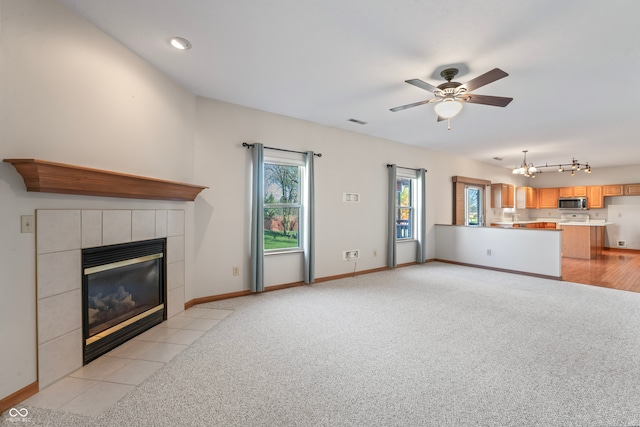 unfurnished living room featuring light carpet, a fireplace, and ceiling fan with notable chandelier