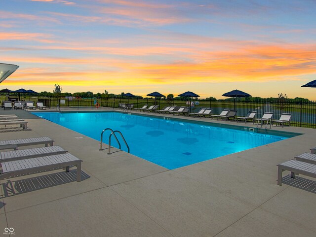 pool at dusk featuring a patio area, fence, and a community pool