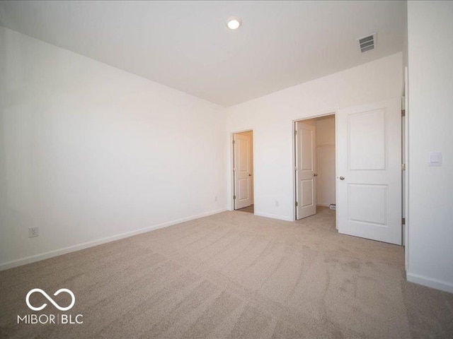 unfurnished bedroom with carpet, a walk in closet, recessed lighting, visible vents, and baseboards