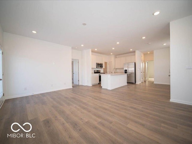 unfurnished living room with baseboards, dark wood-type flooring, a sink, and recessed lighting