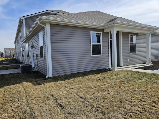 view of side of home featuring central air condition unit, a shingled roof, and a lawn