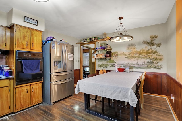 kitchen with wood walls, hanging light fixtures, stainless steel fridge, black oven, and dark hardwood / wood-style flooring