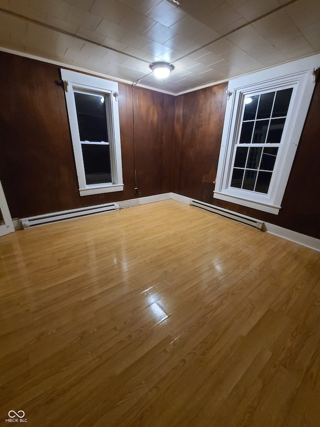 empty room with wood-type flooring, a baseboard radiator, and wood walls