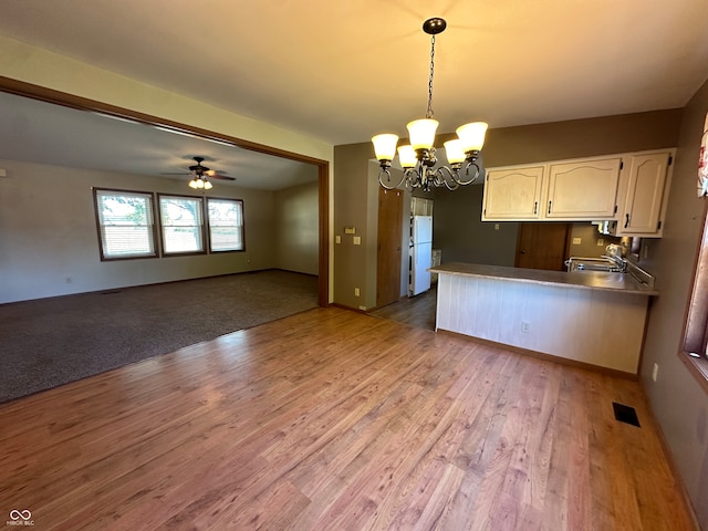 kitchen with hanging light fixtures, white cabinets, ceiling fan with notable chandelier, kitchen peninsula, and light wood-type flooring