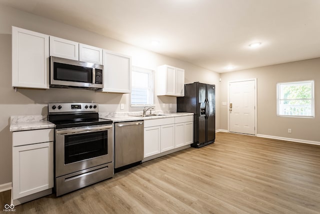 kitchen featuring sink, white cabinetry, stainless steel appliances, light stone countertops, and light hardwood / wood-style floors