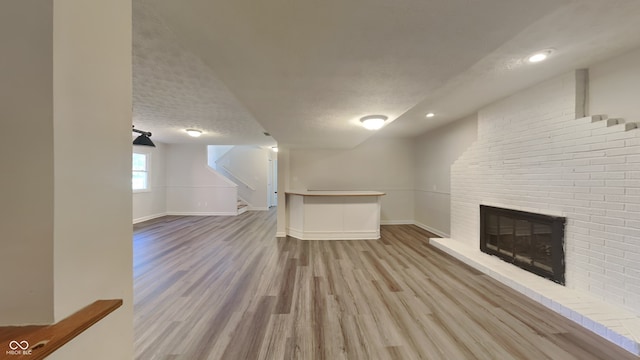 unfurnished living room with wood-type flooring, a textured ceiling, and a brick fireplace