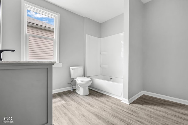 bathroom with wood-type flooring, washtub / shower combination, and toilet