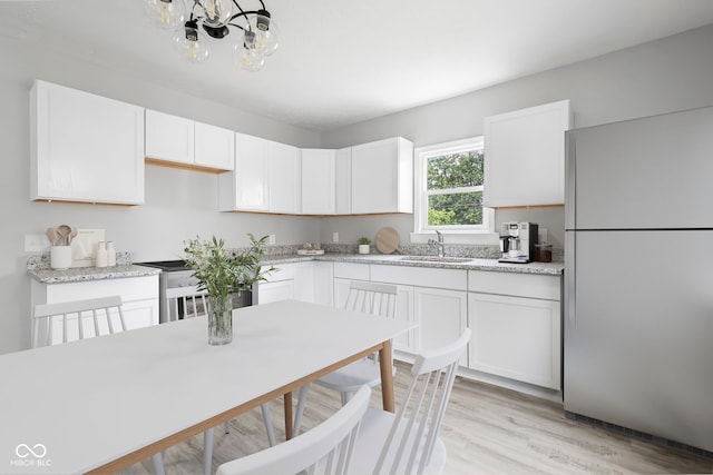 kitchen with light wood-type flooring, sink, a notable chandelier, white cabinetry, and white fridge