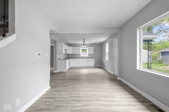 unfurnished living room featuring an inviting chandelier, a wealth of natural light, and light wood-type flooring