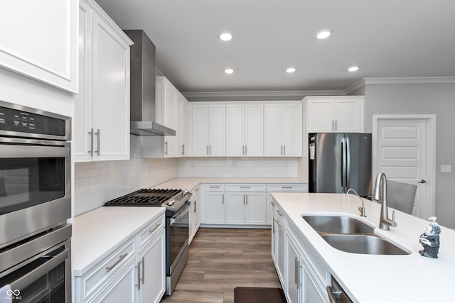 kitchen with sink, white cabinets, wall chimney range hood, appliances with stainless steel finishes, and hardwood / wood-style floors