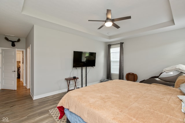 bedroom with ceiling fan, a raised ceiling, and wood-type flooring