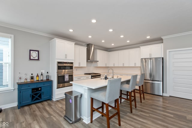 kitchen with a breakfast bar, white cabinetry, wall chimney range hood, appliances with stainless steel finishes, and blue cabinetry