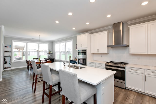 kitchen featuring sink, an island with sink, white cabinets, wall chimney exhaust hood, and appliances with stainless steel finishes