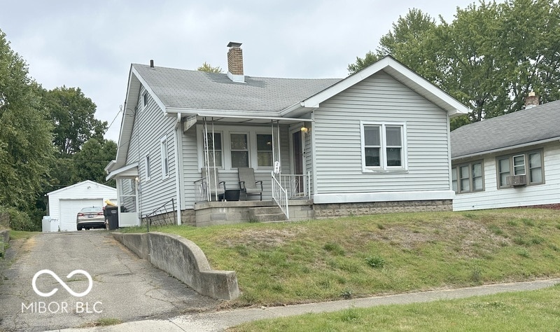 view of front of home with an outdoor structure, a garage, covered porch, and a front lawn