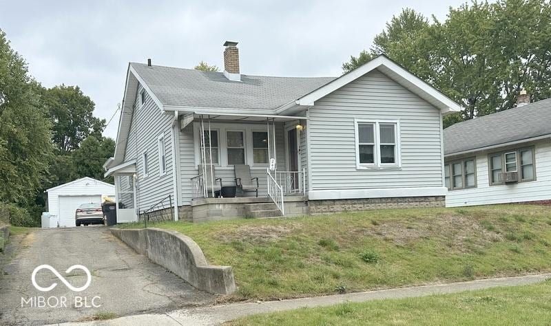 view of front facade with a chimney, a front yard, aphalt driveway, an outbuilding, and a garage