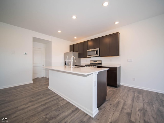 kitchen with sink, appliances with stainless steel finishes, dark brown cabinetry, wood-type flooring, and an island with sink