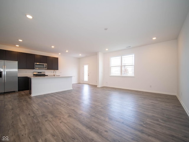 kitchen with stainless steel appliances, dark hardwood / wood-style floors, and a center island with sink