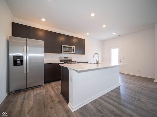 kitchen with sink, dark wood-type flooring, appliances with stainless steel finishes, a kitchen island with sink, and dark brown cabinetry