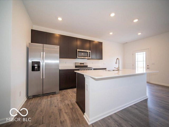 kitchen featuring an island with sink, appliances with stainless steel finishes, dark wood finished floors, and a sink