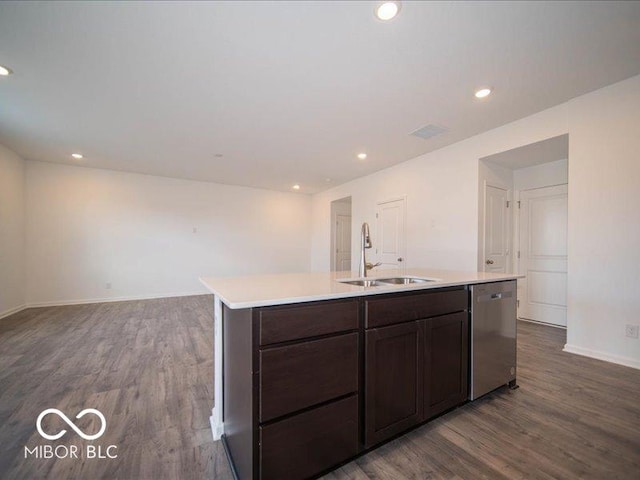 kitchen featuring dark wood-style flooring, light countertops, stainless steel dishwasher, a sink, and an island with sink