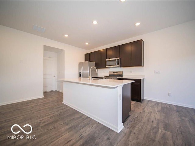 kitchen featuring dark wood-style floors, appliances with stainless steel finishes, a sink, and a kitchen island with sink