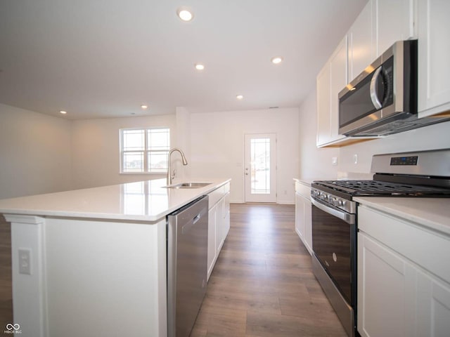 kitchen with appliances with stainless steel finishes, white cabinetry, sink, light wood-type flooring, and an island with sink