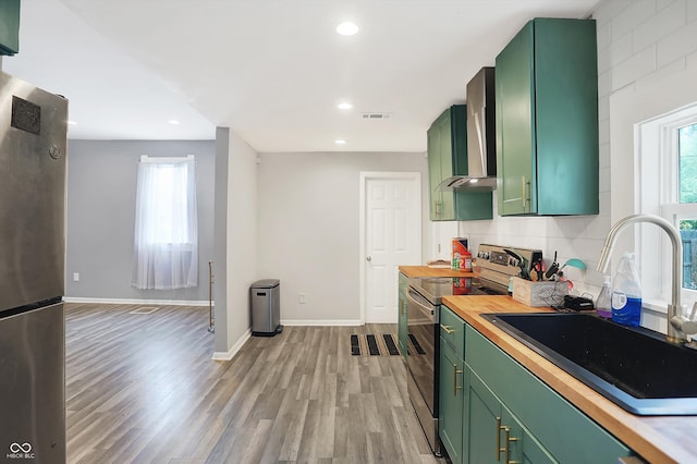 kitchen featuring green cabinetry, appliances with stainless steel finishes, wall chimney exhaust hood, and light hardwood / wood-style flooring