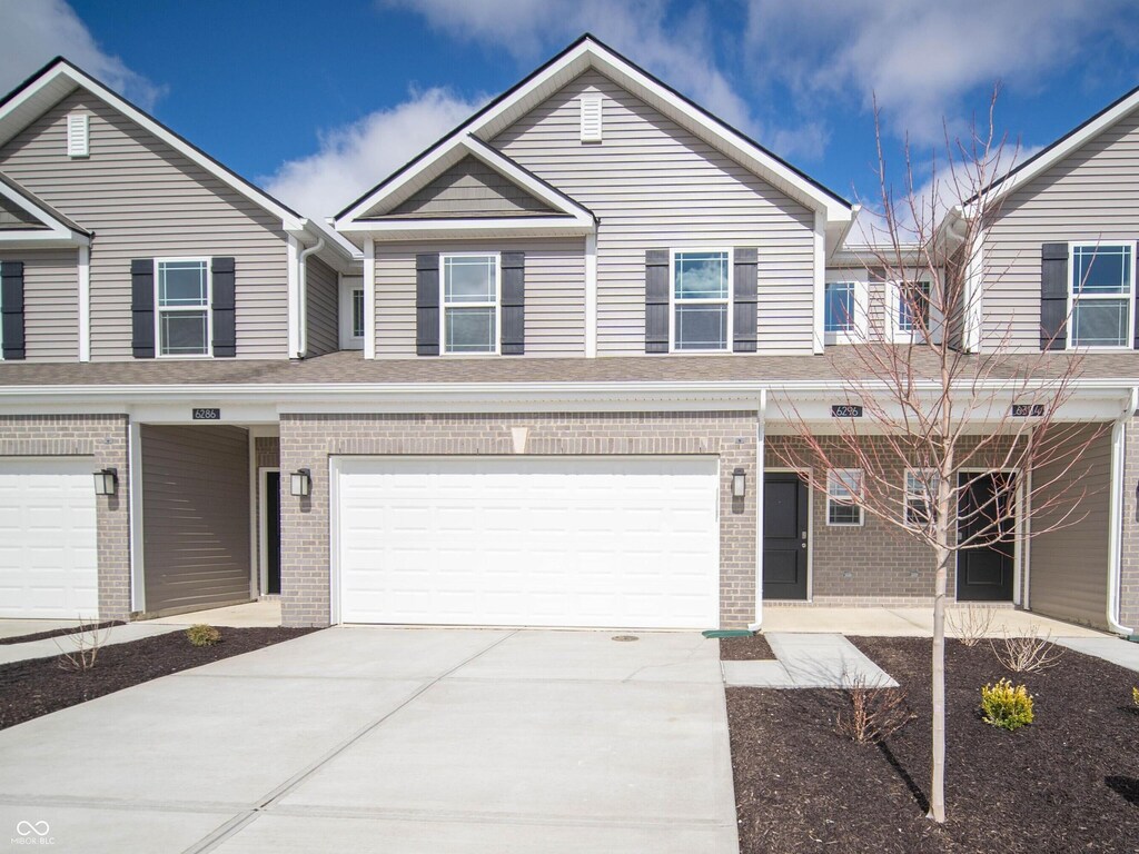 view of property featuring driveway, a garage, and brick siding