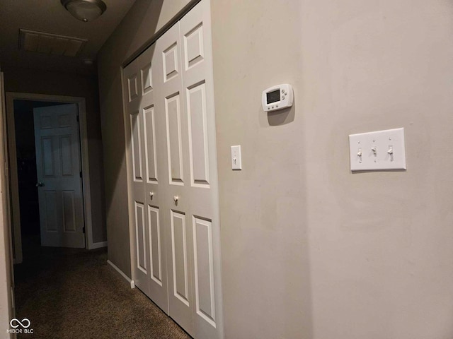 hall with baseboards, visible vents, and dark carpet