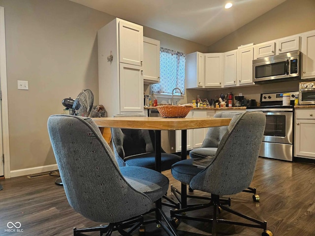 kitchen with appliances with stainless steel finishes, vaulted ceiling, dark wood-style flooring, and white cabinetry