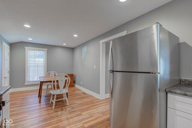 kitchen featuring dark stone countertops, stainless steel refrigerator, light hardwood / wood-style floors, and white cabinetry