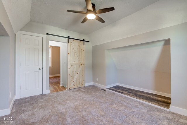 unfurnished bedroom with ceiling fan, carpet flooring, lofted ceiling, and a barn door