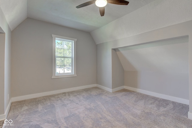 bonus room featuring a textured ceiling, lofted ceiling, light carpet, and ceiling fan