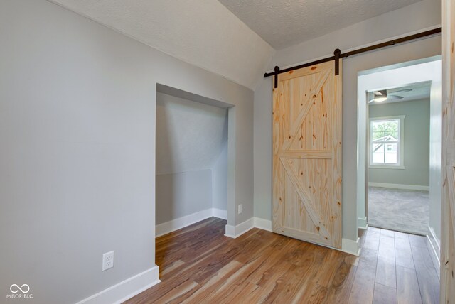 spare room with a barn door, a textured ceiling, light wood-type flooring, and lofted ceiling