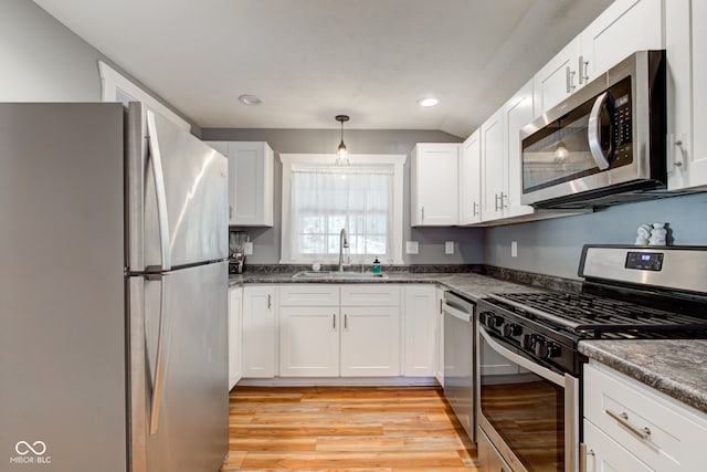 kitchen with white cabinets, appliances with stainless steel finishes, light wood finished floors, a sink, and hanging light fixtures