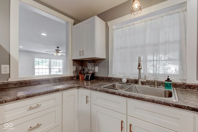 kitchen featuring a sink, ceiling fan, dark countertops, and white cabinetry