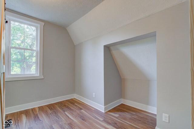 additional living space with a textured ceiling, light hardwood / wood-style floors, and vaulted ceiling