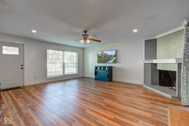 unfurnished living room featuring ceiling fan, a textured ceiling, light hardwood / wood-style flooring, a fireplace, and crown molding