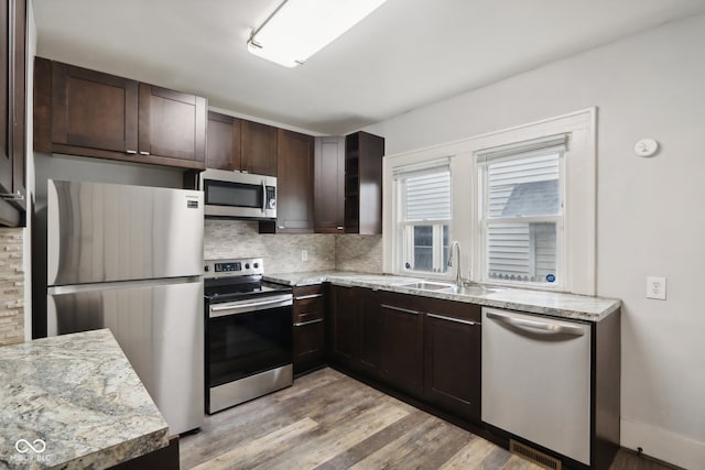 kitchen with light hardwood / wood-style floors, sink, decorative backsplash, stainless steel appliances, and light stone countertops